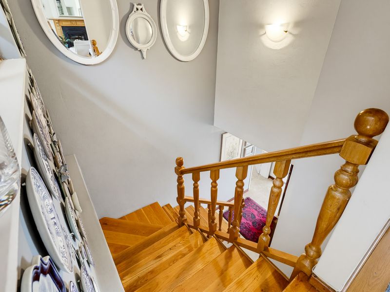 A view looking down a wooden staircase featuring a traditional timber balustrade and wall-mounted lighting fixtures.