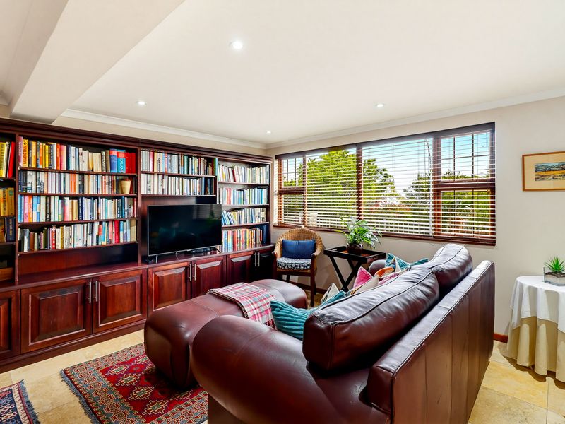 A cozy living room featuring extensive built-in wooden cabinetry, tiled flooring, and large windows with venetian blinds, providing a warm and functional space.