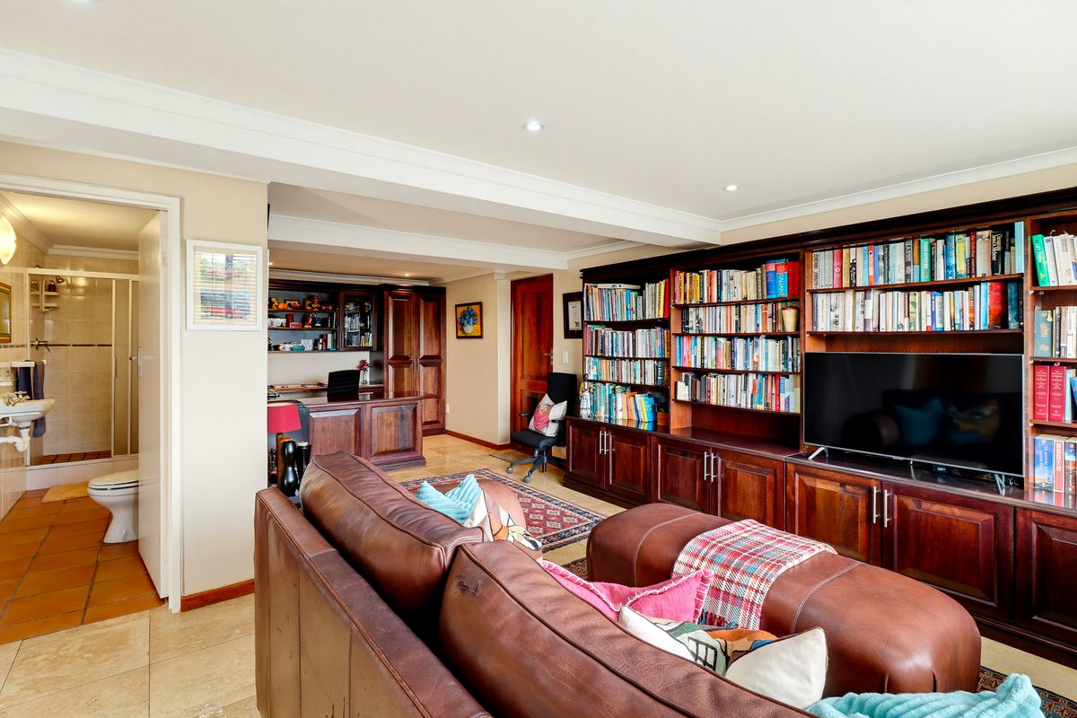 Spacious living area featuring extensive built-in wooden cabinetry and shelving, recessed lighting, and tiled flooring, with an adjacent bathroom visible.