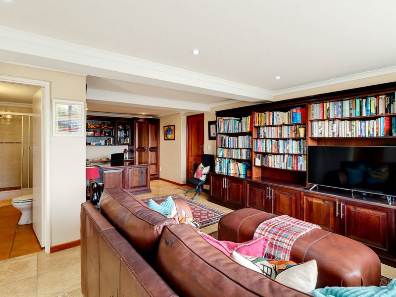 Spacious living area featuring extensive built-in wooden cabinetry and shelving, recessed lighting, and tiled flooring, with an adjacent bathroom visible.