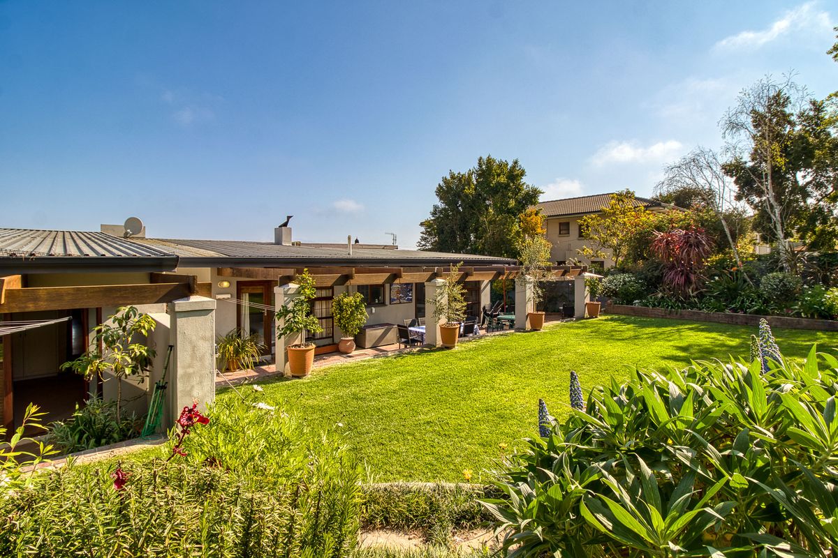 A spacious rear garden featuring a covered patio with timber pergola and masonry pillars, overlooking a well-maintained lawn and established garden beds.