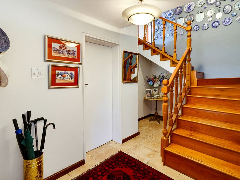 A bright entrance hallway featuring a timber staircase with a traditional balustrade and neutral tiled flooring.