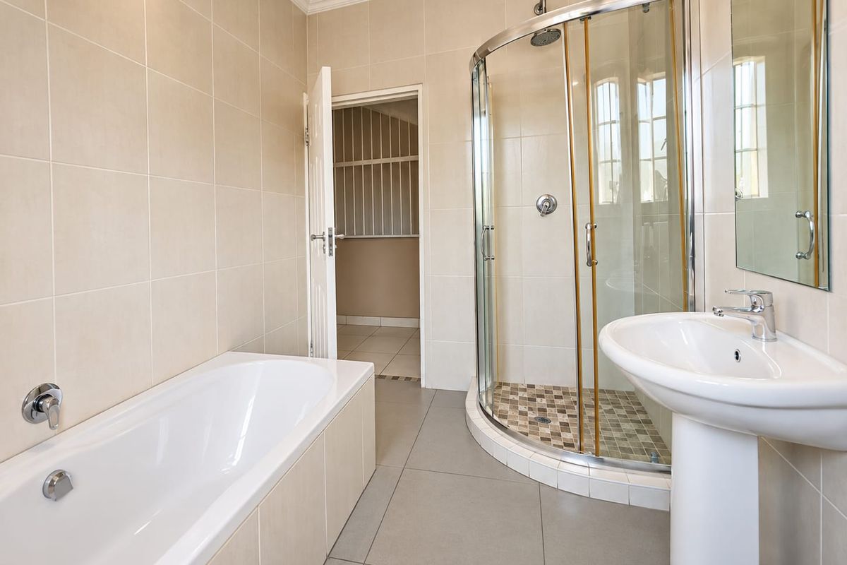 A clean, neutral-toned bathroom featuring a built-in bathtub, a separate curved glass shower enclosure, and a pedestal washbasin with modern fixtures.