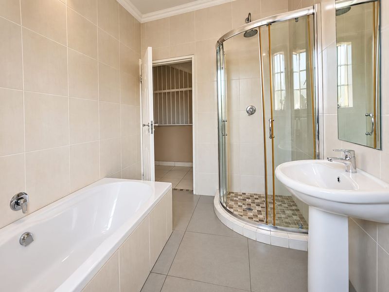 A clean, neutral-toned bathroom featuring a built-in bathtub, a separate curved glass shower enclosure, and a pedestal washbasin with modern fixtures.