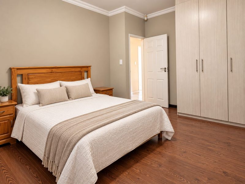 A well-maintained bedroom featuring warm-toned laminate flooring, neutral wall paint, and ample built-in cupboard storage with modern finishes.