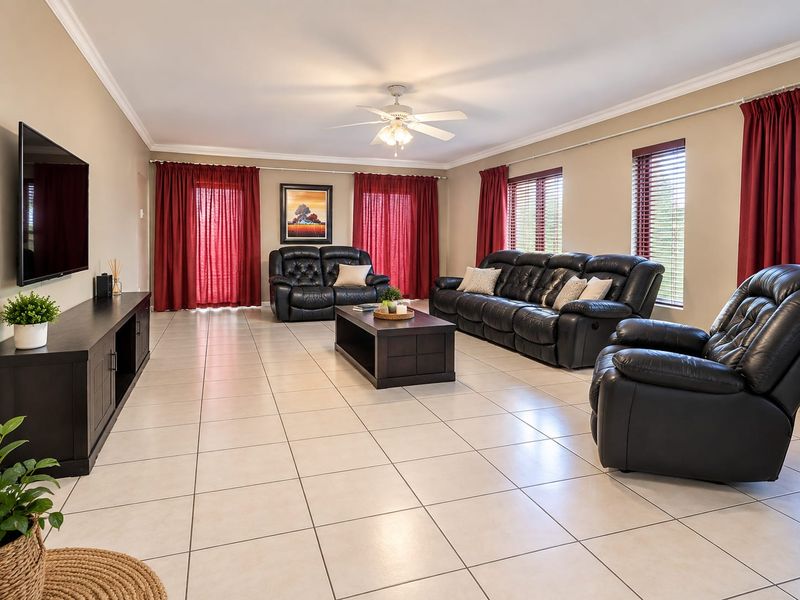 Spacious living room featuring neutral tiled flooring, crown molding, a central ceiling fan, and large windows with venetian blinds.