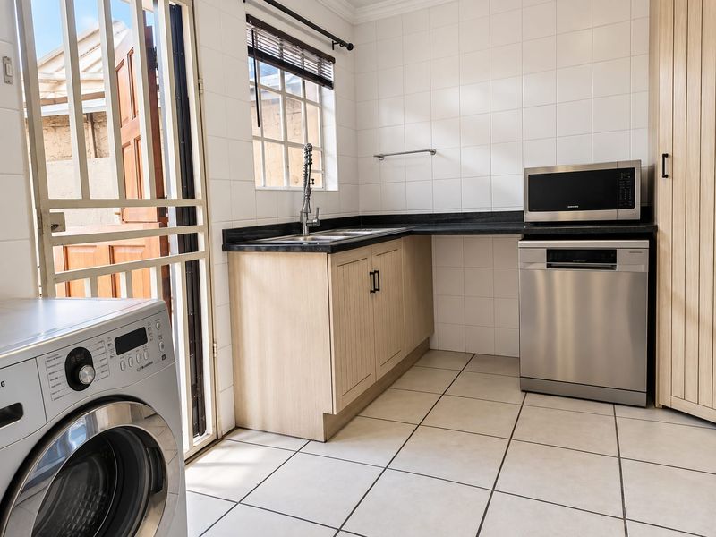 A functional laundry area featuring built-in cabinetry, laminate countertops, a stainless steel sink, and tiled finishes with direct access to the exterior.