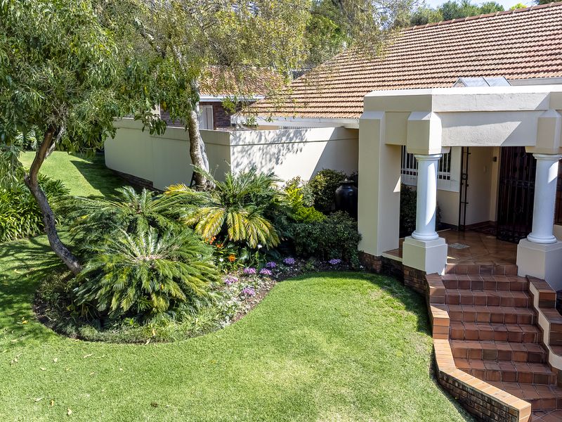 A well-maintained front entrance featuring tiled steps, decorative columns, and a landscaped garden with a surrounding boundary wall.