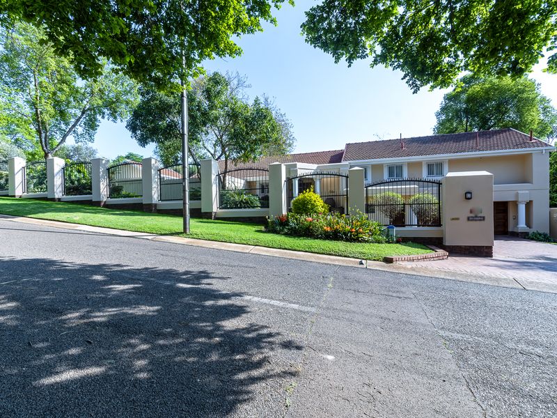 Front elevation of a well-maintained house featuring a paved driveway, secure wrought iron fencing, and established garden landscaping.
