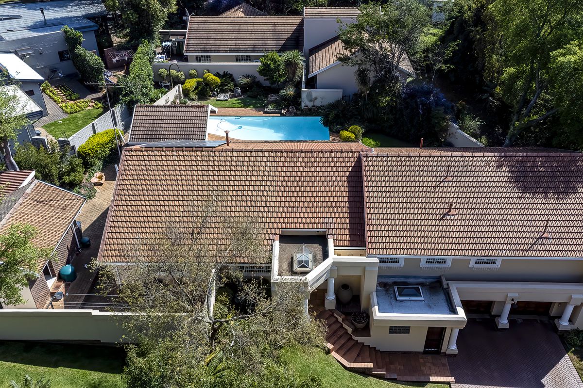 Aerial view of the property showcasing the main residence, tiled roof, swimming pool, and surrounding landscaped garden area.