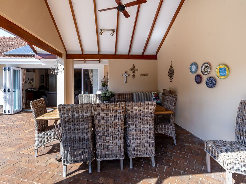 A spacious covered patio featuring exposed timber rafters, a ceiling fan, and brick paved flooring, seamlessly connecting to the interior via bi-fold doors.