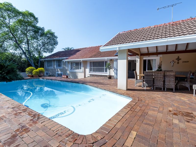 Outdoor entertainment area featuring a swimming pool and a spacious covered patio with brick paving, ideal for relaxation and hosting guests.