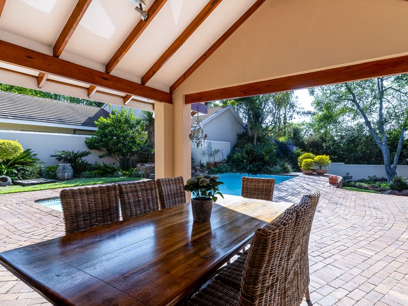 A covered outdoor patio featuring exposed timber beams and vaulted ceilings, overlooking a private swimming pool and landscaped garden area.