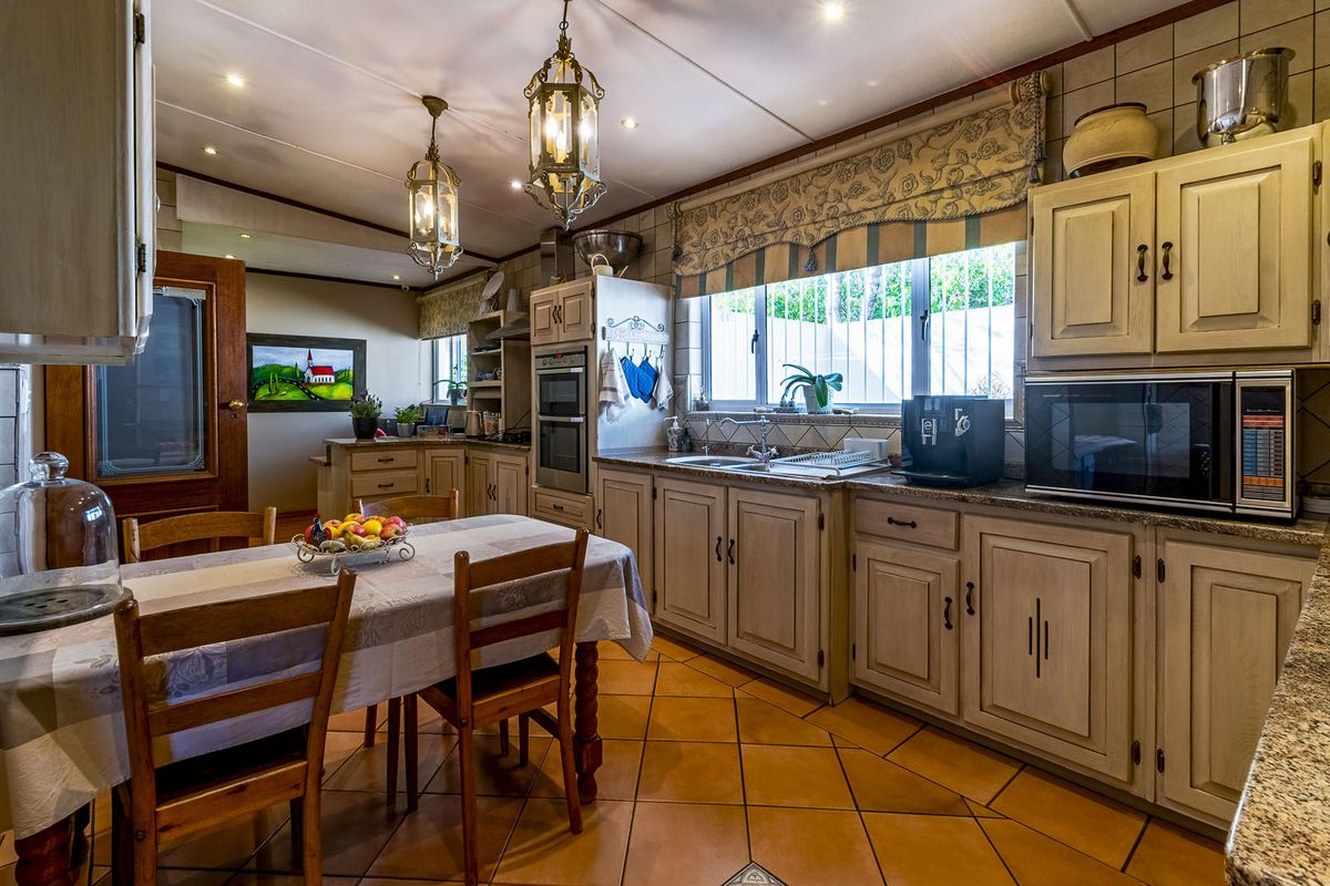 A traditional kitchen featuring light-toned cabinetry, granite countertops, built-in oven, and ceramic tile flooring, offering a functional layout with integrated dining space.