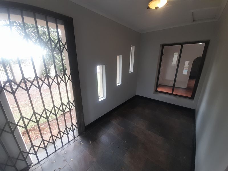 An empty entrance hall featuring dark tiled flooring, a security gate, and multiple windows providing natural light.