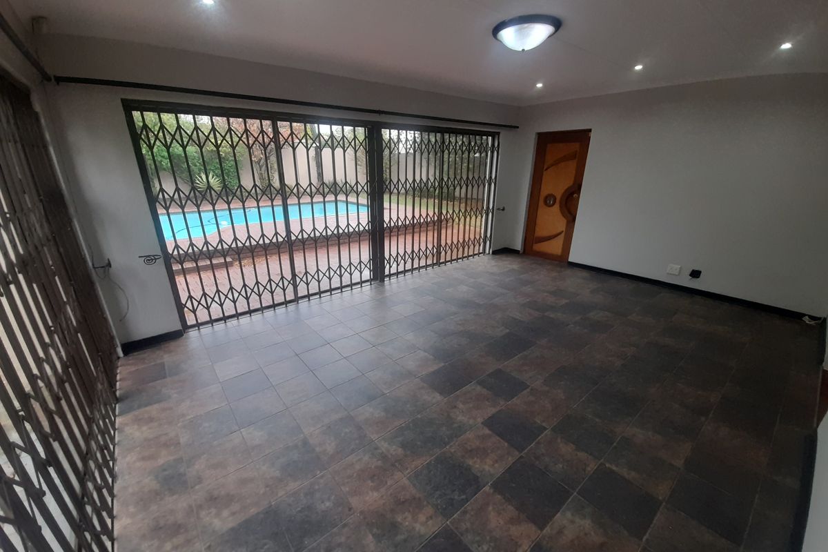 An empty living area featuring dark tiled flooring, recessed lighting, and large sliding doors with security gates providing direct access to the pool area.