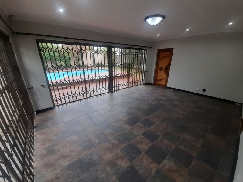 An empty living area featuring dark tiled flooring, recessed lighting, and large sliding doors with security gates providing direct access to the pool area.