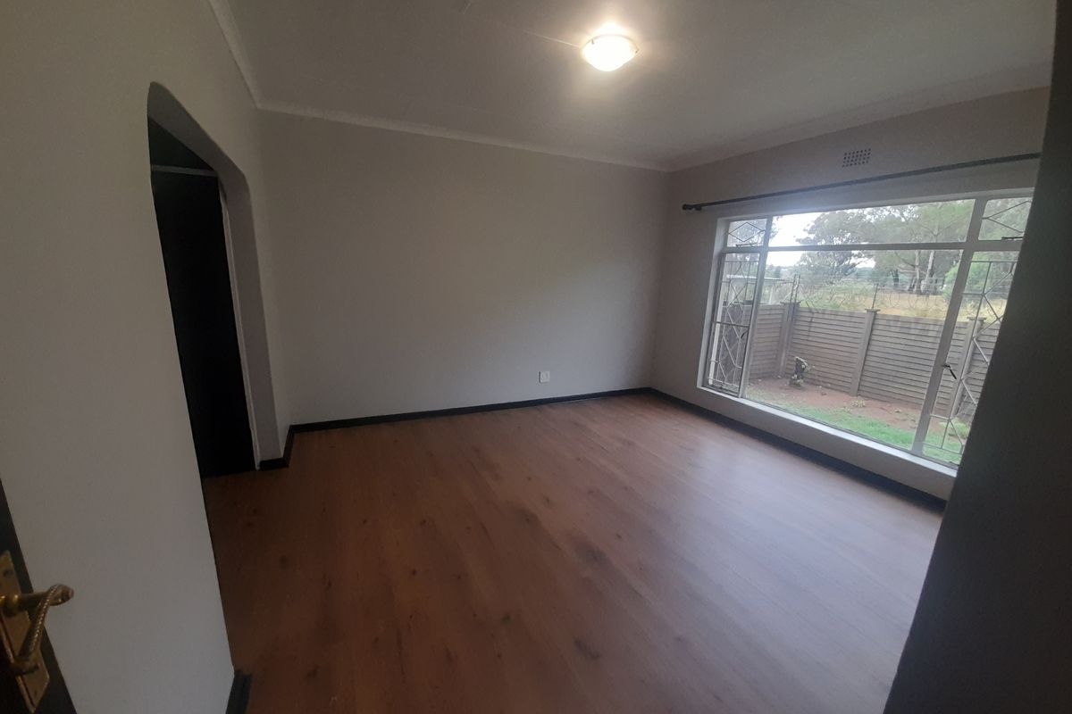 A bright, empty bedroom featuring modern laminate flooring, a large window with security bars, and a neutral color palette.