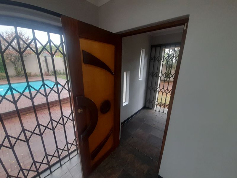 An entrance area featuring tiled flooring, a decorative wooden front door, and security gates providing a view of the outdoor pool area.