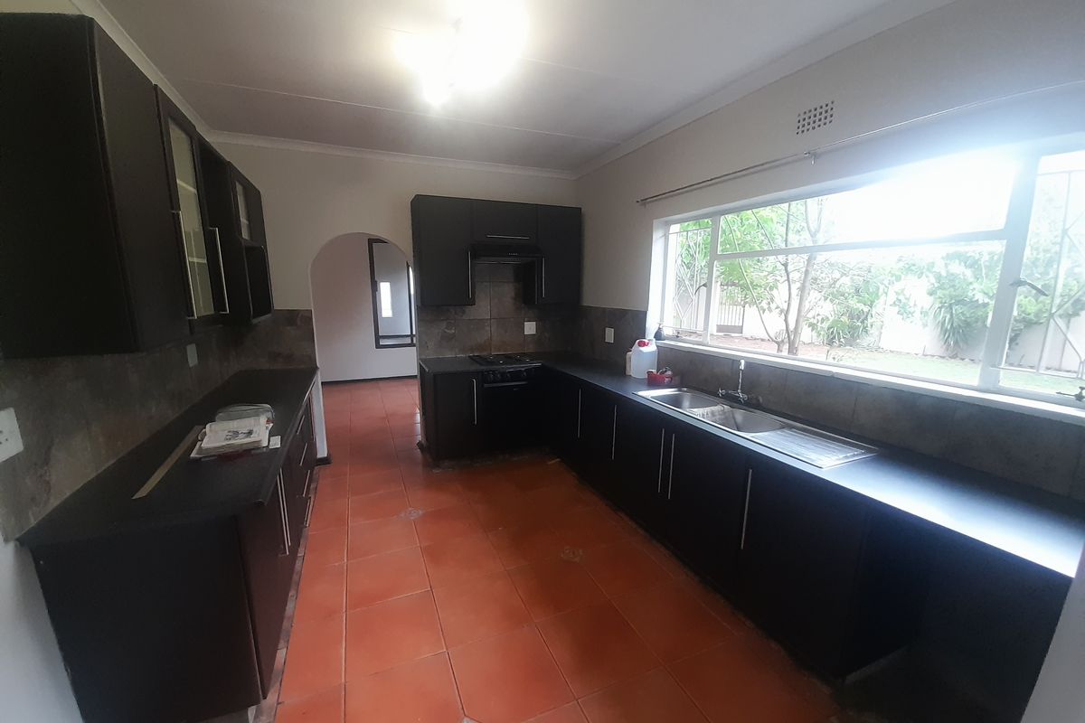 Spacious kitchen featuring dark built-in cabinetry, a double bowl sink, integrated oven and hob, and large windows overlooking the garden.