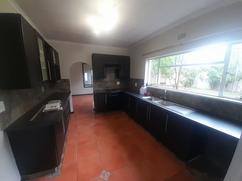 Spacious kitchen featuring dark built-in cabinetry, a double bowl sink, integrated oven and hob, and large windows overlooking the garden.