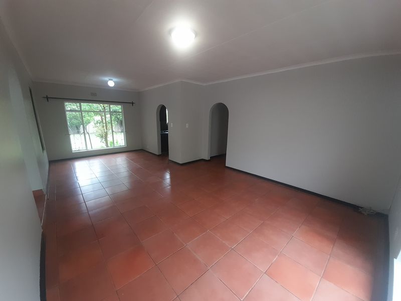 A spacious, empty living area featuring terracotta-style floor tiles, neutral walls, and arched doorways leading to adjacent rooms.