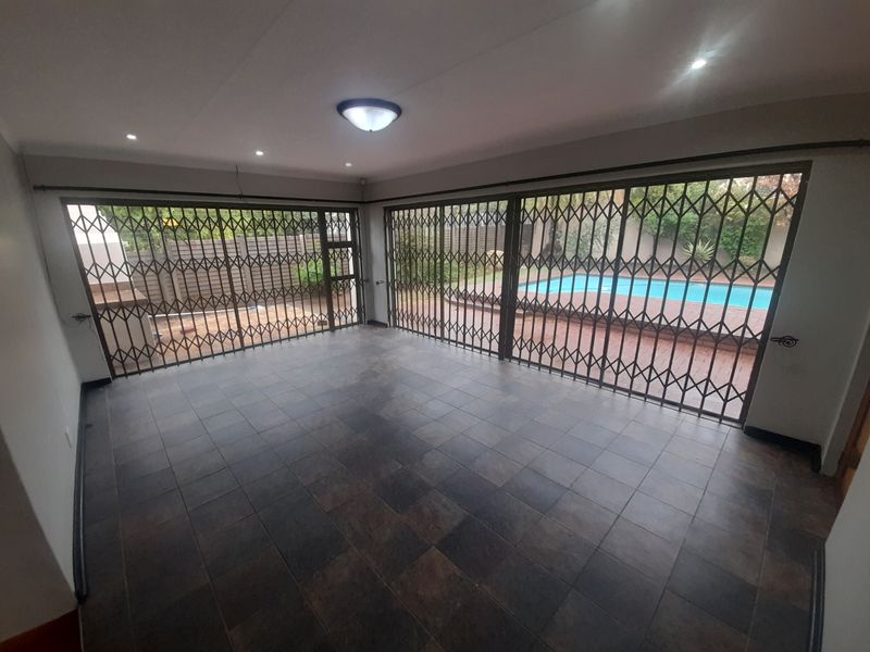 Spacious living area featuring tiled flooring and large sliding glass doors with security gates, offering direct access to the outdoor pool area.
