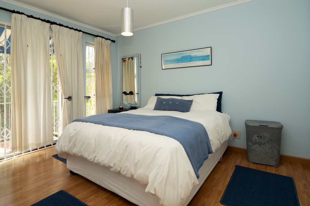 A well-lit bedroom featuring laminate flooring and a sliding glass door with security gate, providing direct access to an outdoor area.
