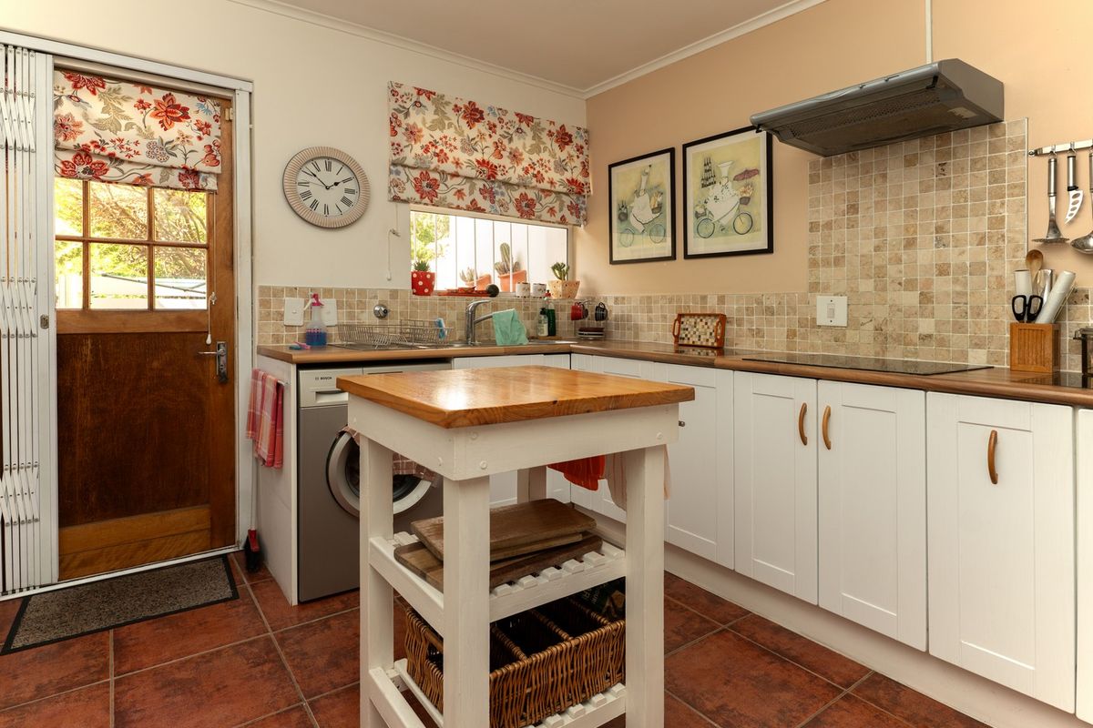 A functional kitchen featuring white cabinetry, timber countertops, tiled backsplash, and integrated hob with extractor fan, providing direct access to the exterior.
