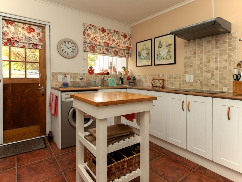 A functional kitchen featuring white cabinetry, timber countertops, tiled backsplash, and integrated hob with extractor fan, providing direct access to the exterior.