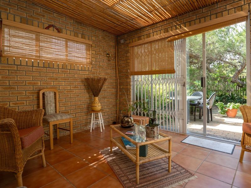 A sunlit enclosed patio featuring exposed brick walls, a bamboo ceiling, and terracotta floor tiles, with direct access to the garden through a sliding door.