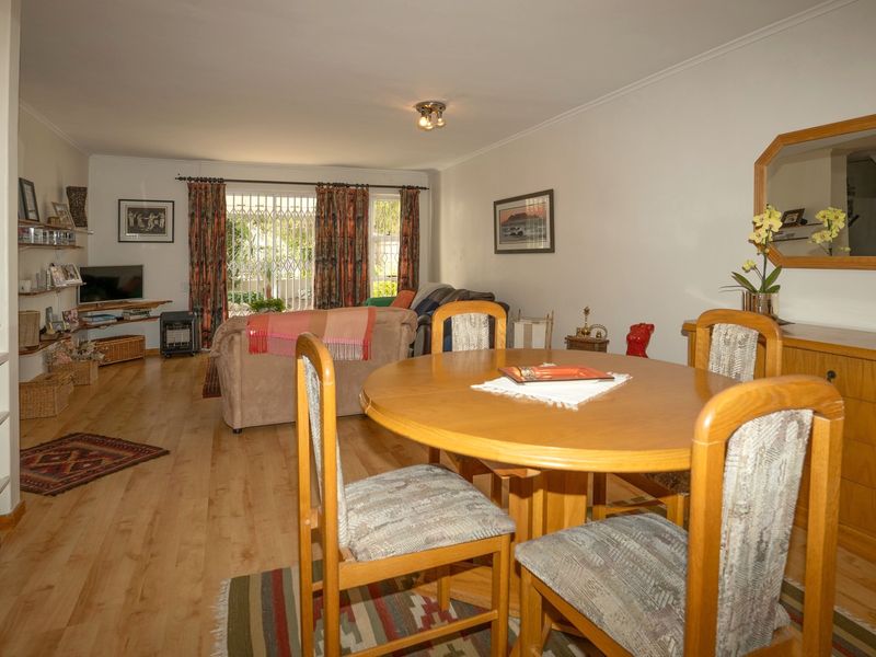 Open plan living and dining area featuring light wood-look laminate flooring and access to the exterior through a security gate.