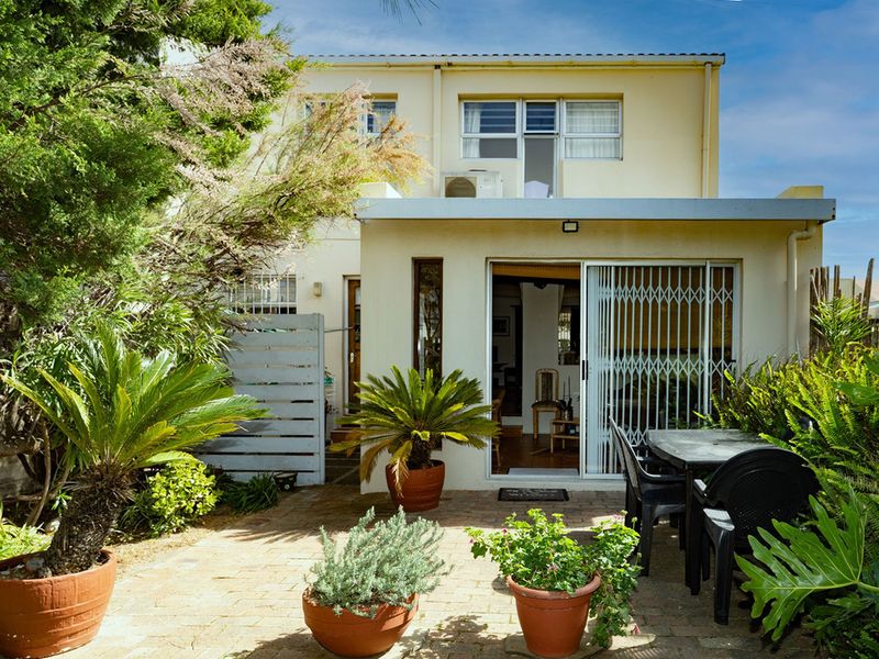 Rear view of the property featuring a paved patio area, sliding glass doors with security gates, and established garden landscaping.