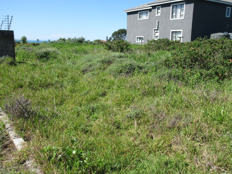 A view of a vacant residential plot featuring overgrown grass, perimeter electric fencing, and a water storage tank adjacent to a neighboring property.