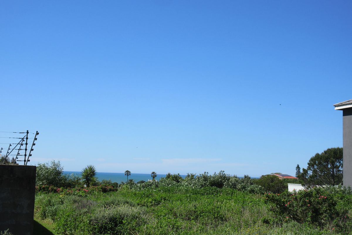 A scenic view overlooking coastal vegetation with a distant ocean horizon, featuring perimeter electric fencing on the property boundary.