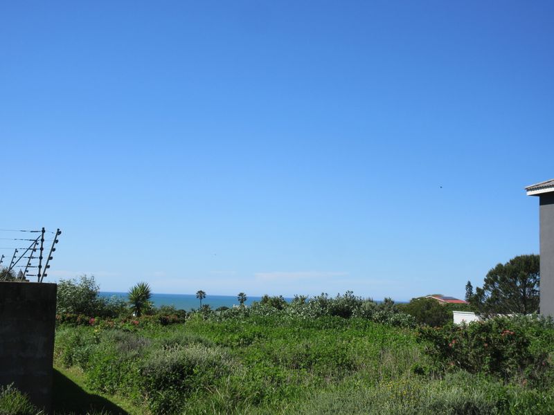 A scenic view overlooking coastal vegetation with a distant ocean horizon, featuring perimeter electric fencing on the property boundary.