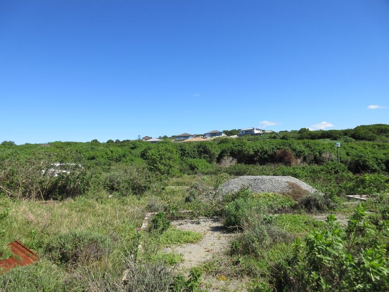A vacant residential plot featuring overgrown vegetation and a visible concrete foundation slab, situated in a quiet neighborhood setting.