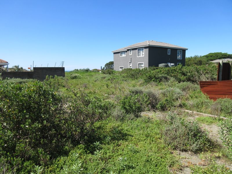 A view of a vacant residential plot featuring overgrown vegetation, perimeter walling with electric fencing, and adjacent residential structures.