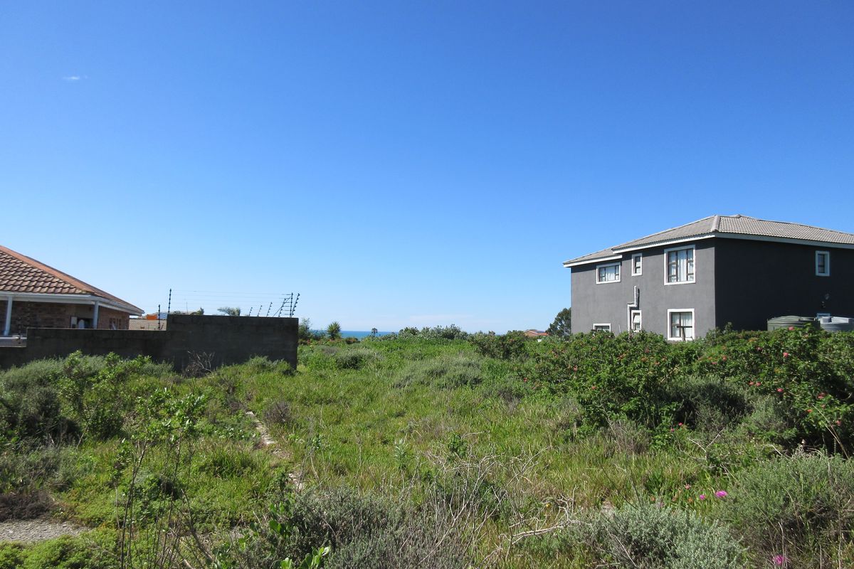 A vacant residential plot featuring natural vegetation, boundary walls with electric fencing, and views of neighboring properties.