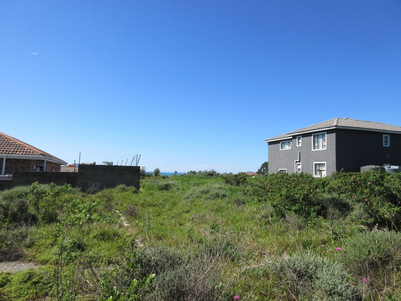 A vacant residential plot featuring natural vegetation, boundary walls with electric fencing, and views of neighboring properties.