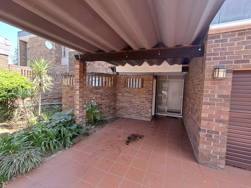 A covered front entrance area featuring brick walls, tiled flooring, and a secure gate, providing a functional and sheltered access point to the townhouse.
