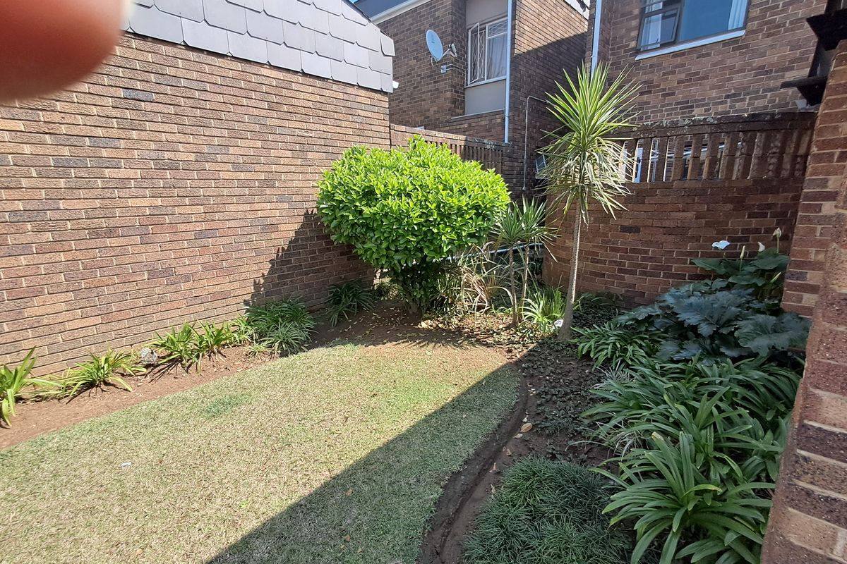 A private rear garden area featuring a small lawn and established garden beds enclosed by brick boundary walls.