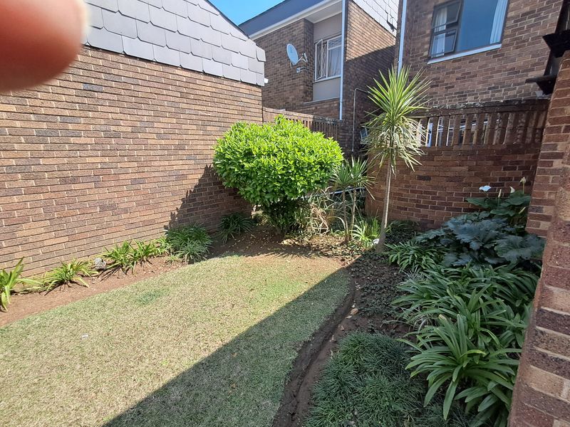 A private rear garden area featuring a small lawn and established garden beds enclosed by brick boundary walls.