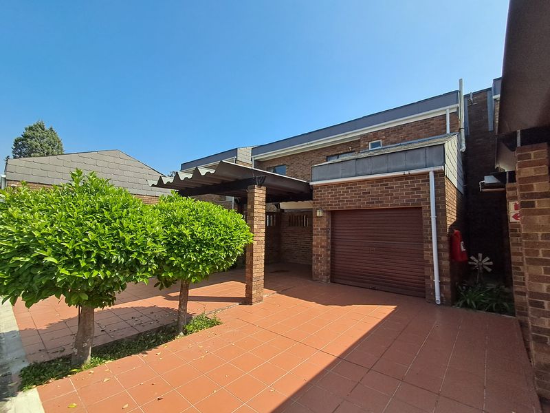 Front exterior view of the townhouse featuring a brick facade, tiled driveway, and a covered carport with a secure roller garage door.