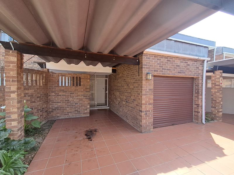 Front exterior view of the townhouse featuring a brick facade, tiled carport area, and a secure roller garage door.