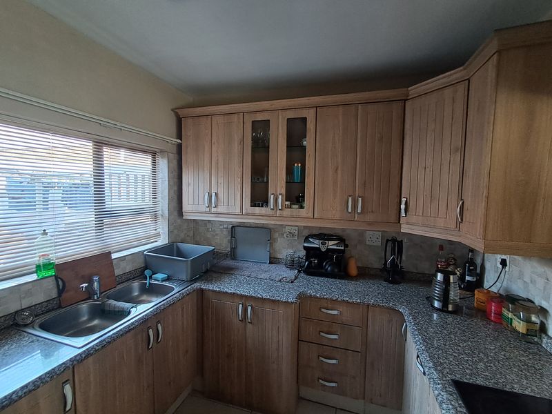 A functional kitchen featuring light wood-tone cabinetry, granite countertops, a double basin stainless steel sink, and a tiled backsplash with natural light.
