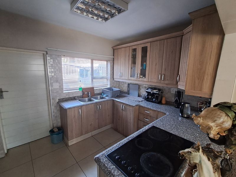A functional kitchen featuring laminate cabinetry, granite countertops, a double basin sink, and an integrated electric hob with tiled flooring.
