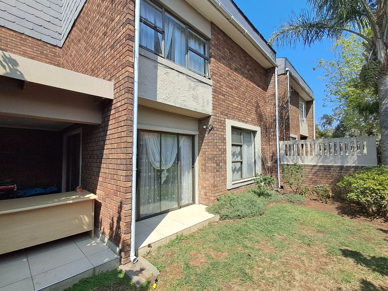 Rear view of the townhouse featuring a brick facade, a small tiled patio area, and access to the garden through sliding glass doors.