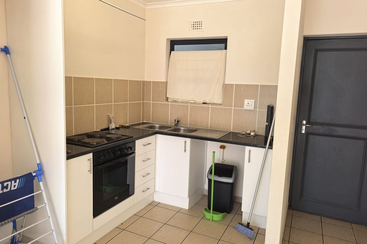 A functional kitchen featuring built-in cabinetry, a black electric oven and hob, stainless steel sink, and neutral tiled backsplash and flooring.