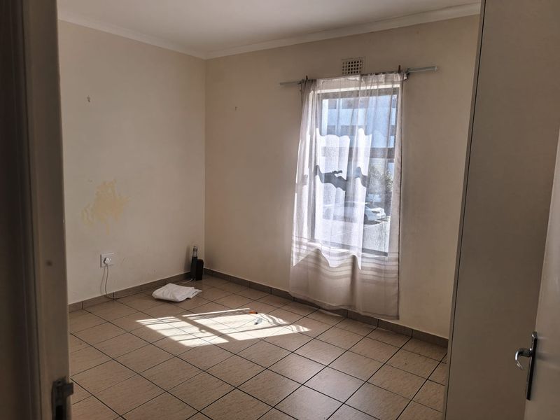 An empty bedroom featuring tiled flooring and a window, requiring minor cosmetic updates such as wall repairs and fresh paint to enhance its appeal.